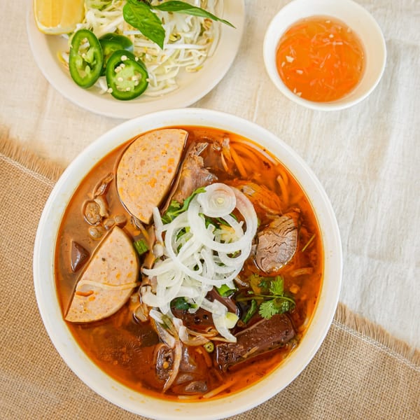 Overhead view of a vibrant Vietnamese bun bo Hue soup with various meats, onions, and herbs.